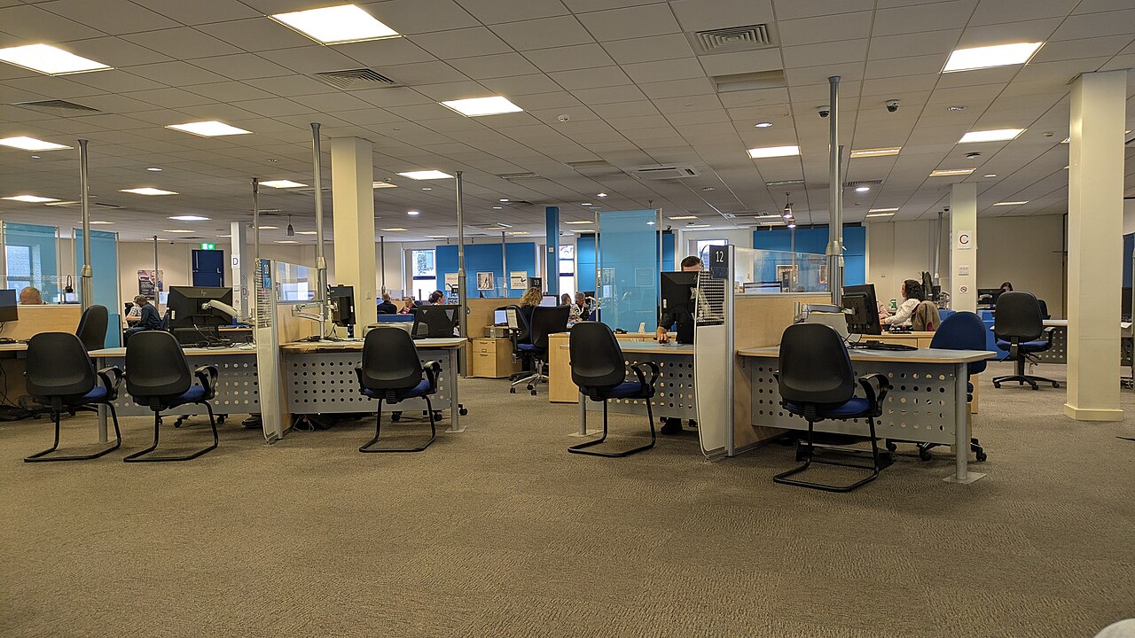 Inside a jobcentre, with rows of desks, computers, and people getting help